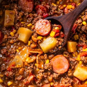 Cowboy stew in a pot with a wooden spoon resting inside.