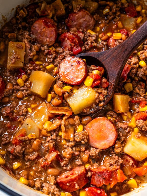 Cowboy stew in a pot with a wooden spoon resting inside.