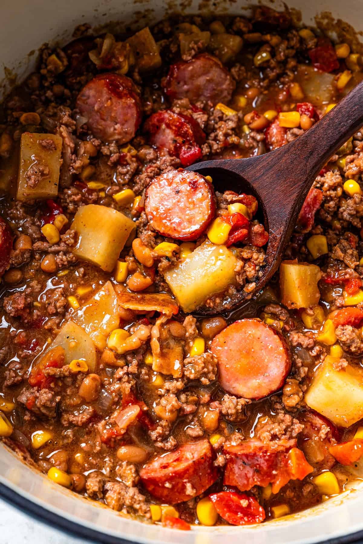 Cowboy stew in a pot with a wooden spoon resting inside.