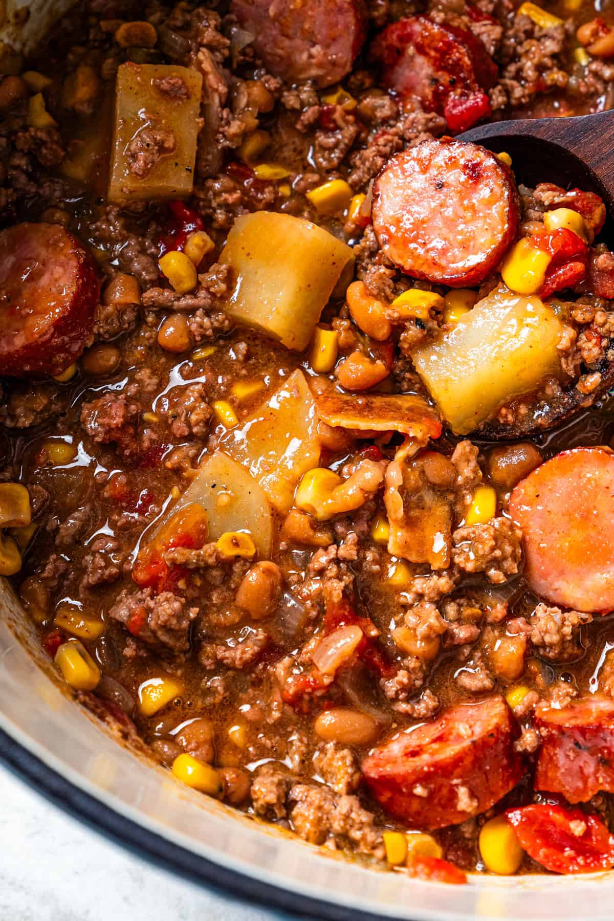 Close-up shot of a stew with sliced sausages, ground beef, and potatoes.