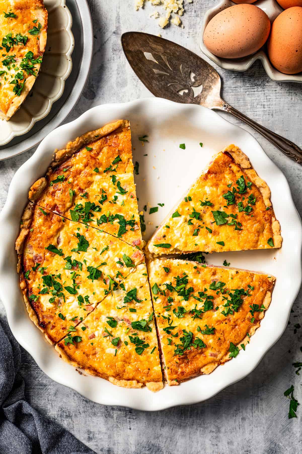 Overhead view of ham and cheese quiche garnished with herbs and cut into slices in a pie plate.