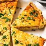 Ham and cheese quiche slices garnished with herbs in a pie plate.