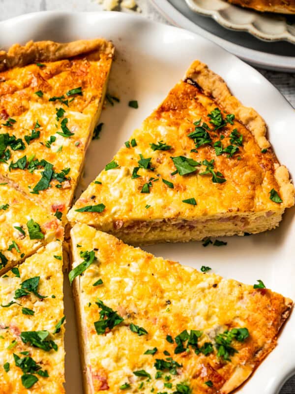 Ham and cheese quiche slices garnished with herbs in a pie plate.