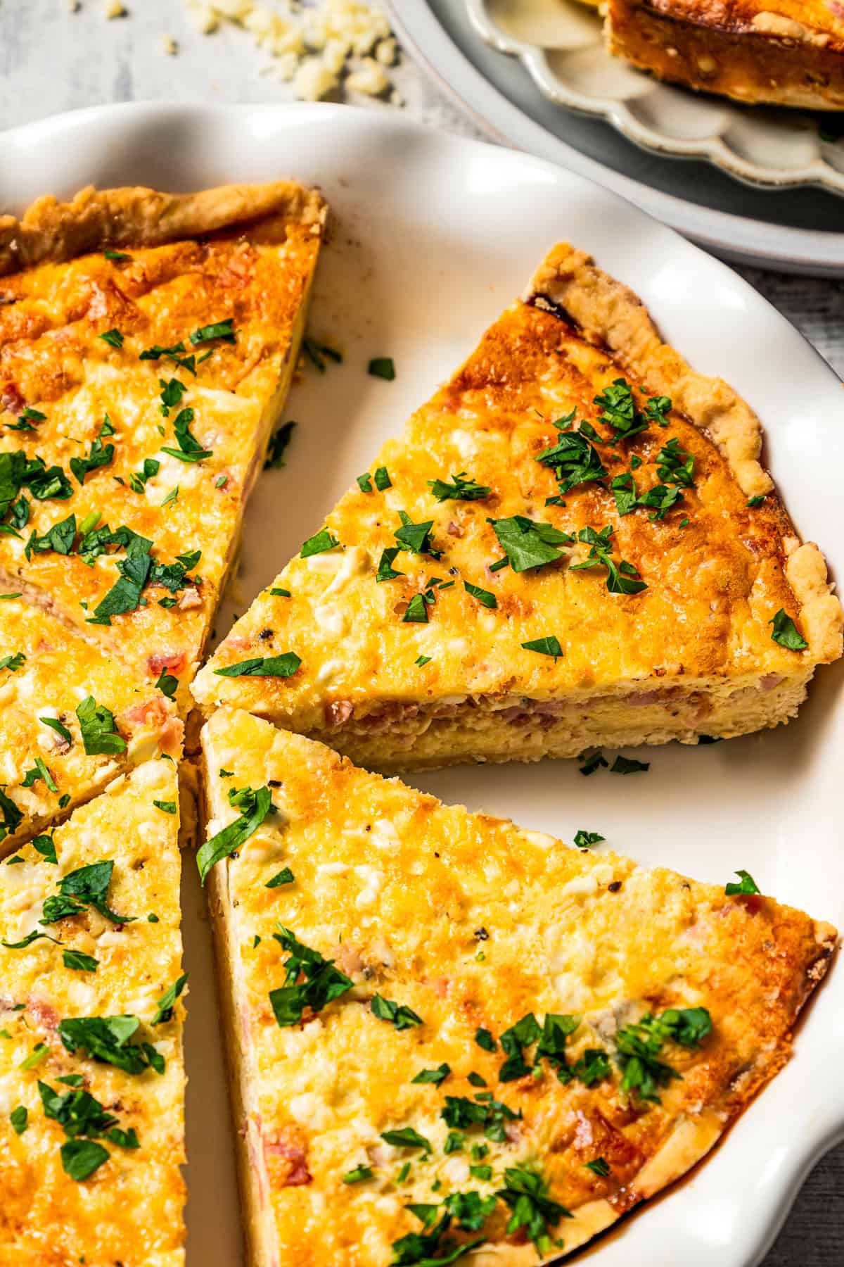 Ham and cheese quiche slices garnished with herbs in a pie plate.