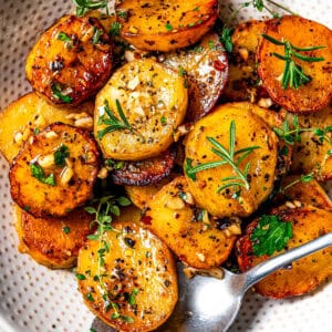 Melting potatoes served in a bowl and garnished with fresh herbs.