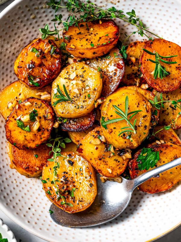 Melting potatoes served in a bowl and garnished with fresh herbs.