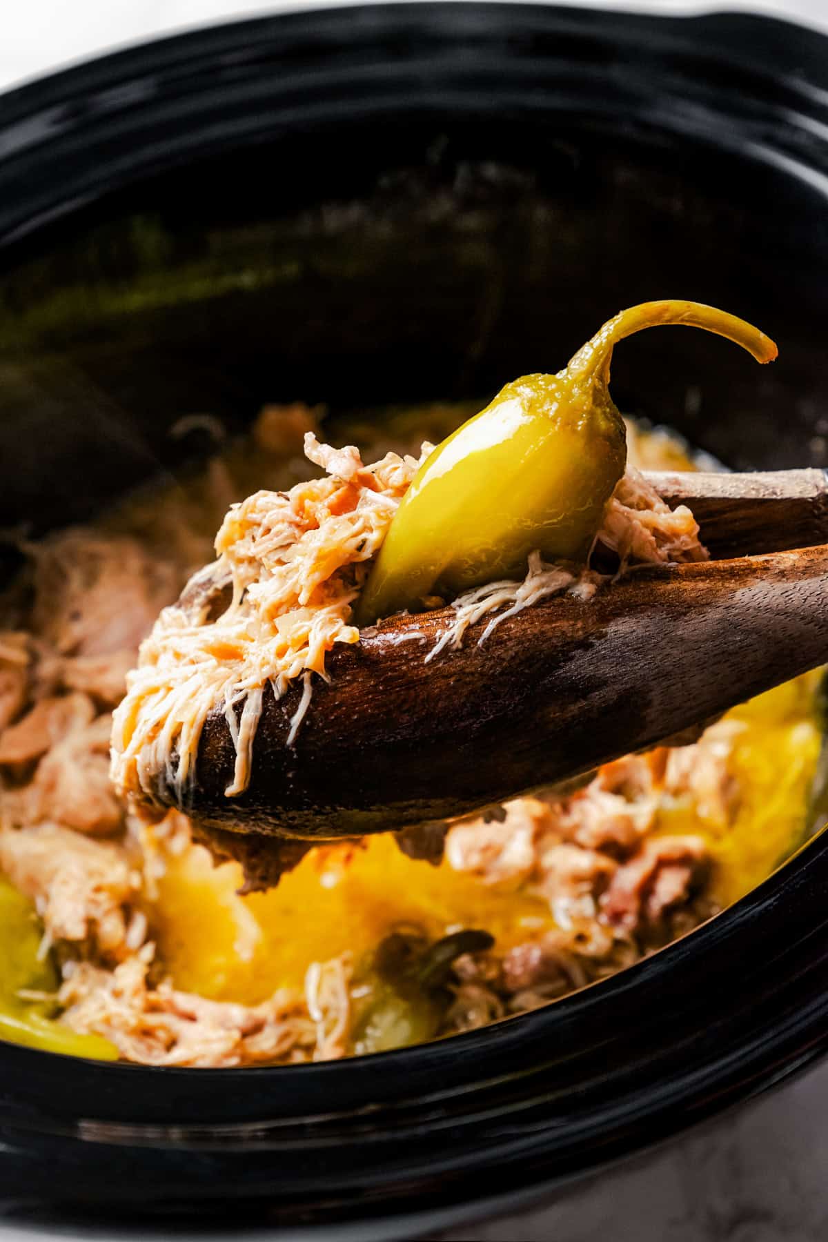 Tongs lifting a serving of Mississippi chicken from the slow cooker.