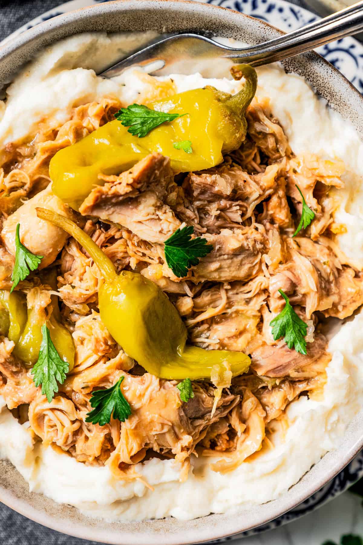 Close-up photo of shredded Mississippi chicken and pepperoncini served over mashed potatoes.