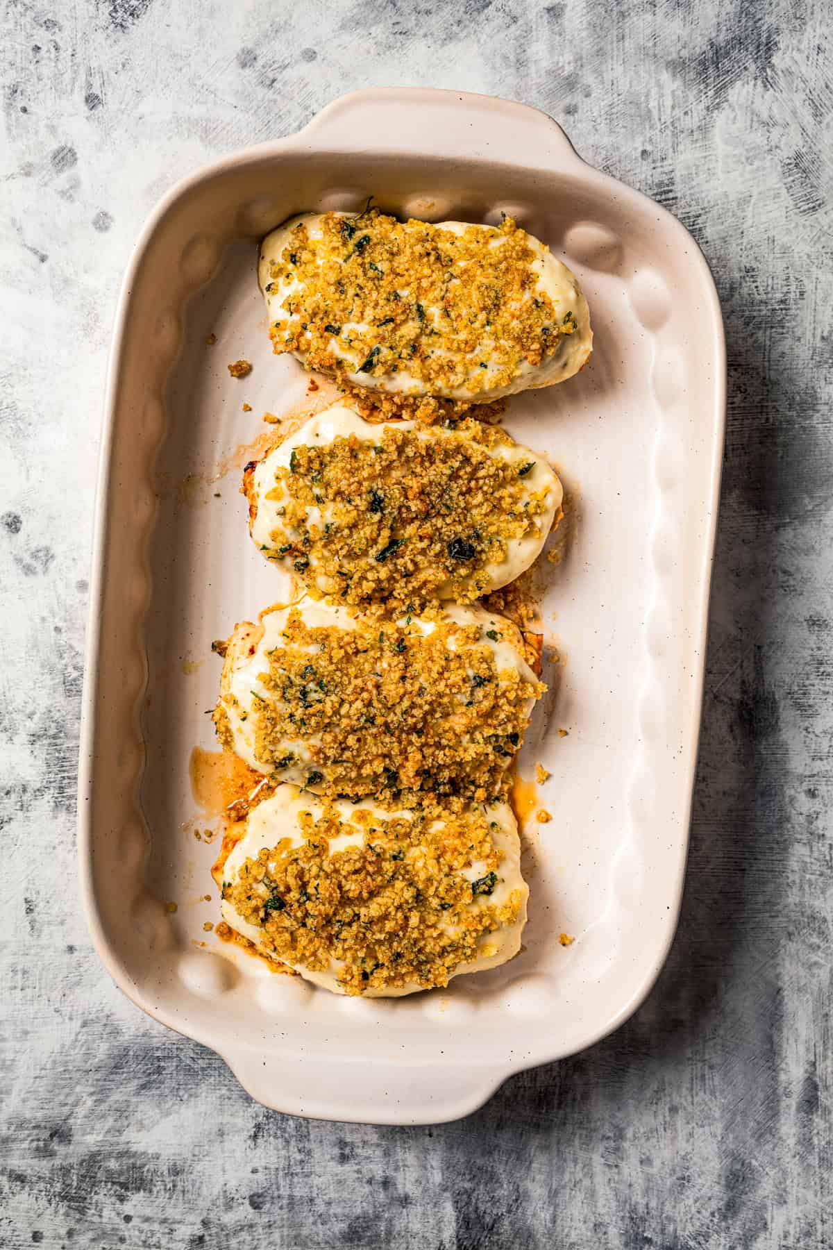 Chicken breasts covered with parmesan sauce and seasoned breadcrumbs in a baking dish.