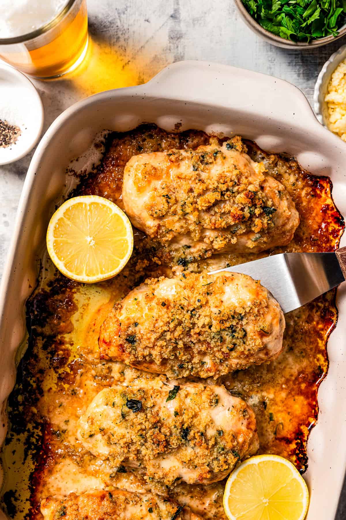 A spatula is lifting up a parmesan crusted chicken breast from a baking dish.