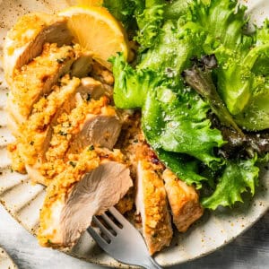 Sliced parmesan chicken served on a dinner plate with a green salad and lemon wedges.