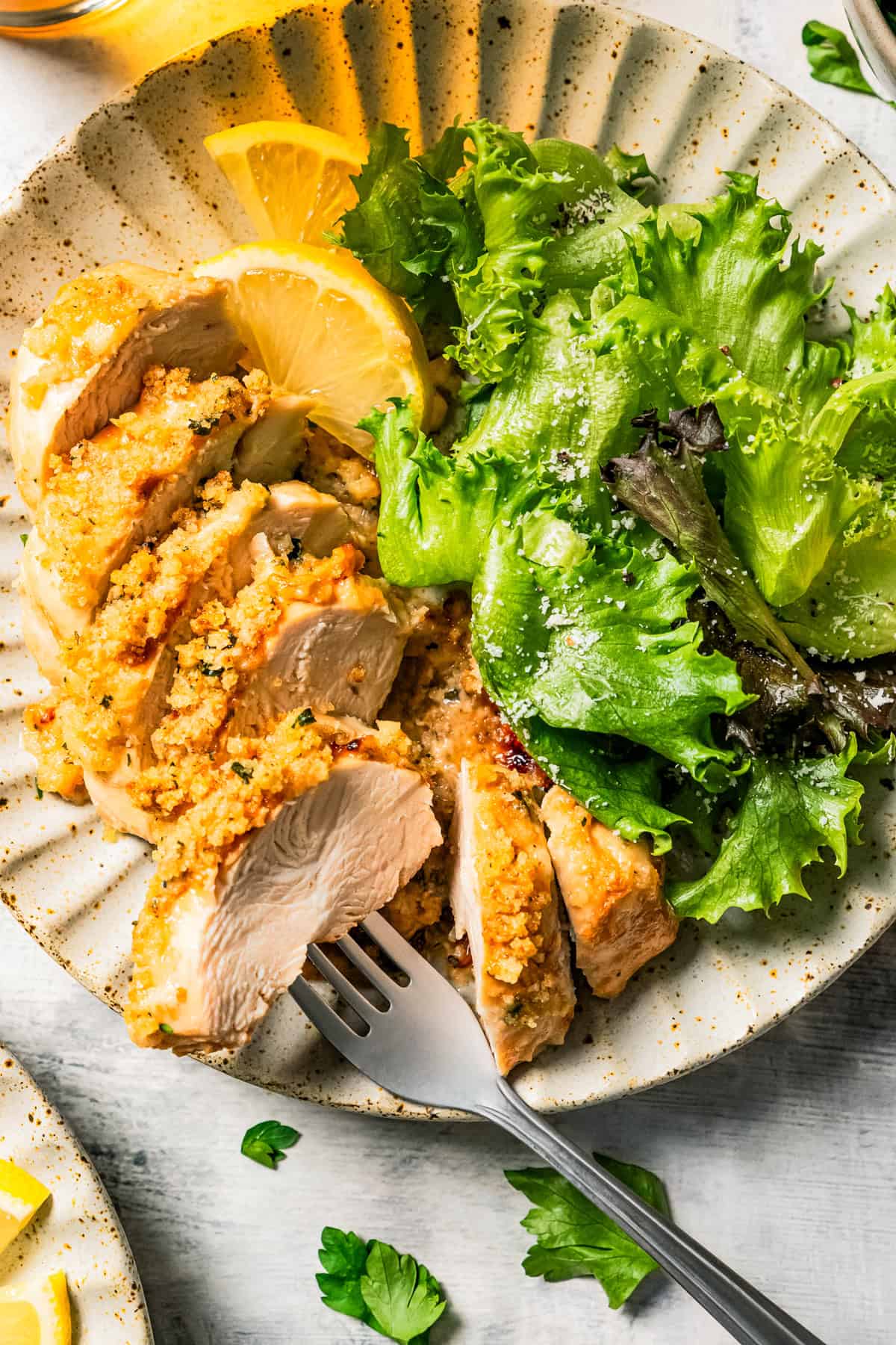 Sliced parmesan chicken served on a dinner plate with a green salad and lemon wedges.