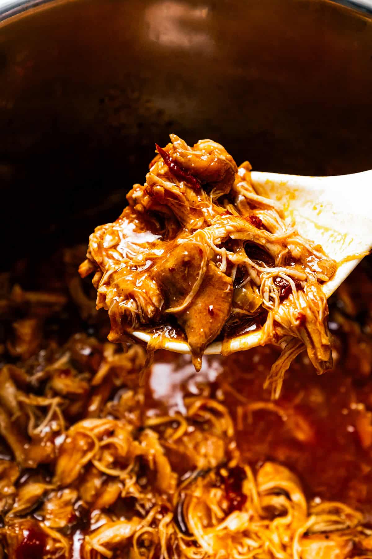 A spoon scooping chicken tinga from a pot.