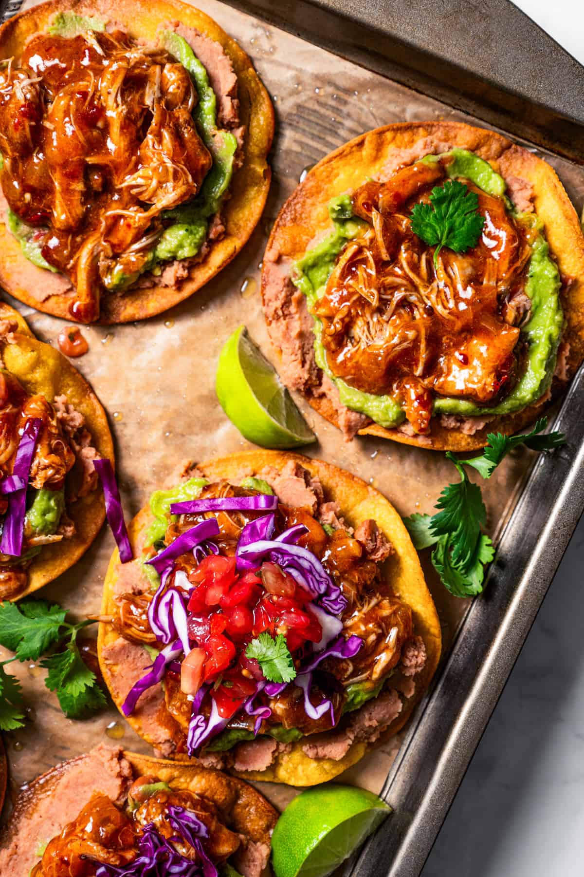 Partially assembled tostadas de tinga on a lined baking sheet.