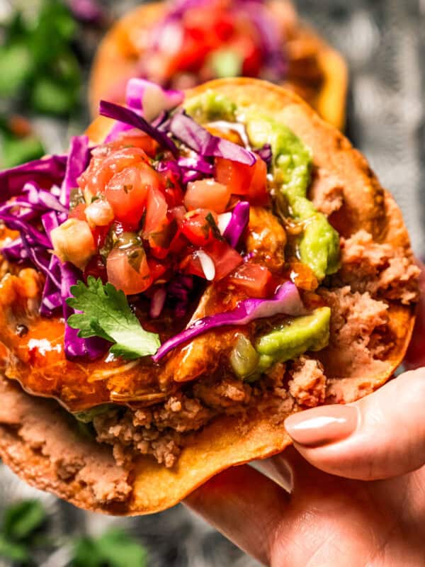 Close up of a hand holding up a tostada de tinga piled with toppings.