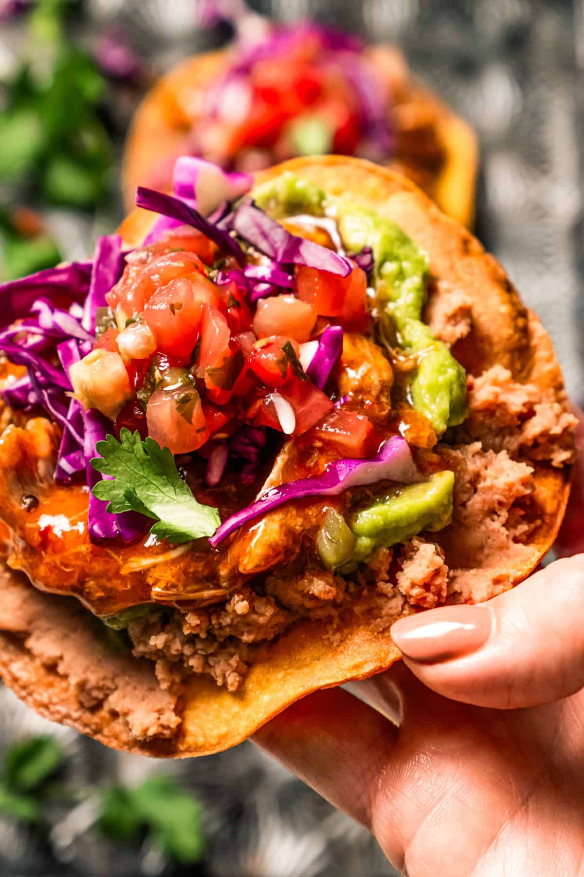 Close up of a hand holding up a tostada de tinga piled with toppings.