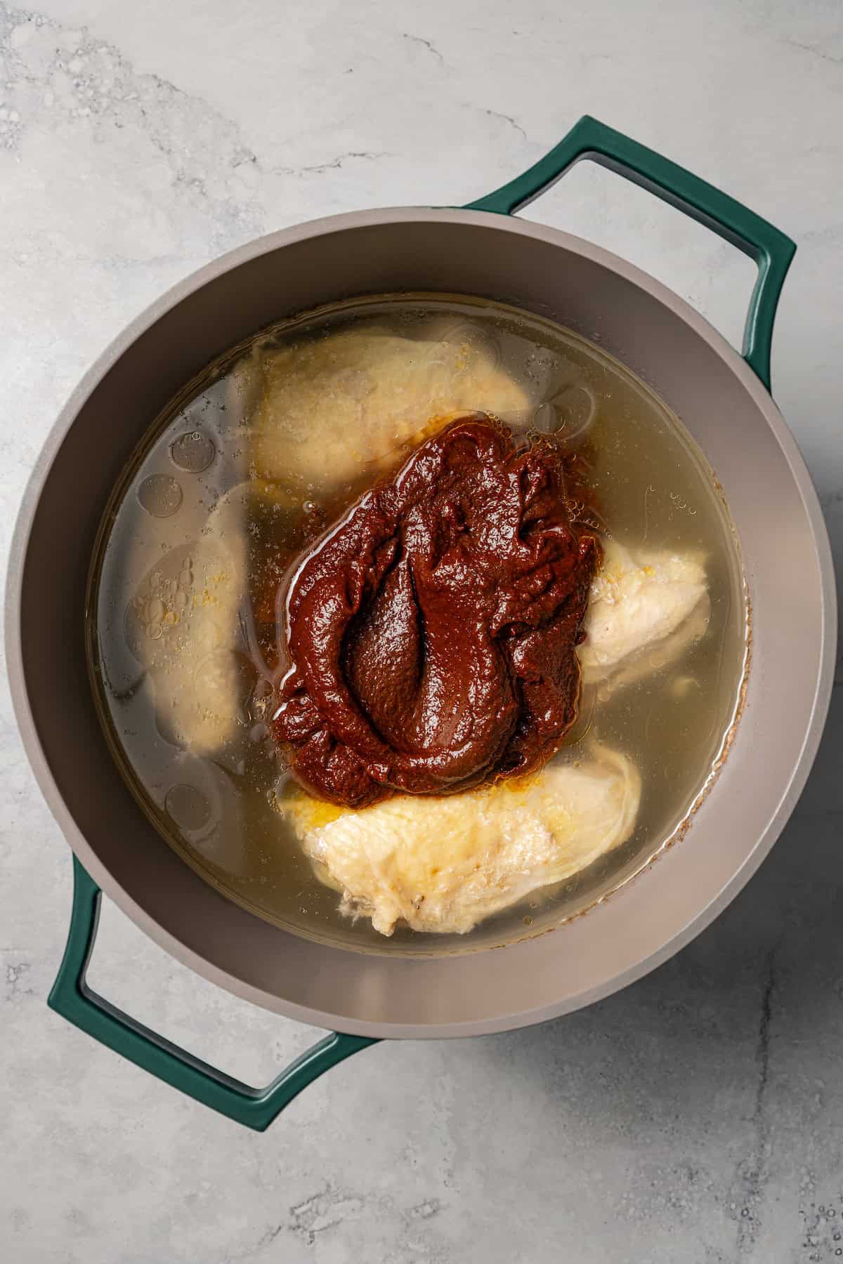 Blended birria sauce added to a pot with poached chicken breasts in broth.