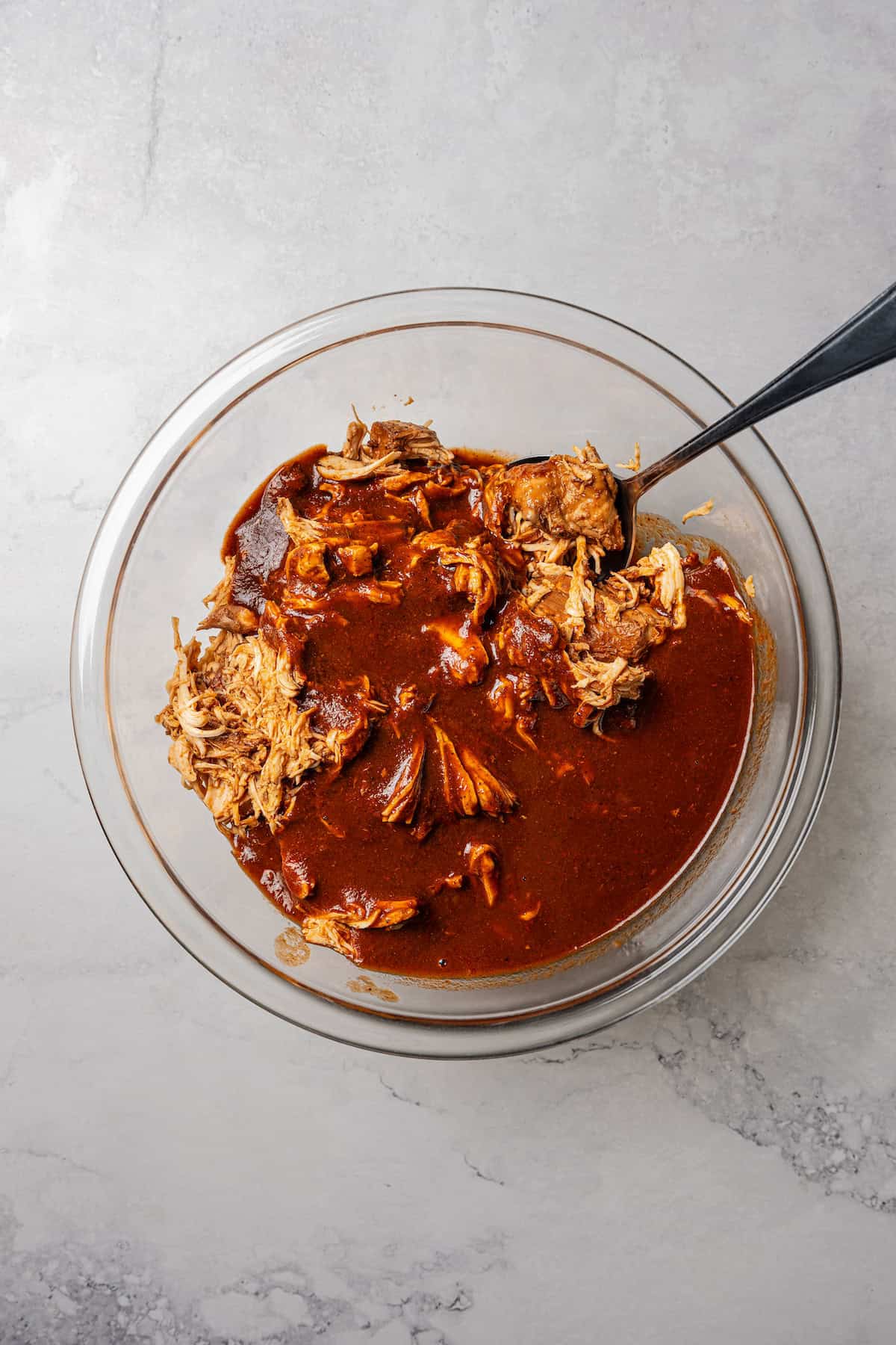 Chicken combined with birria sauce in a glass bowl with a spoon.