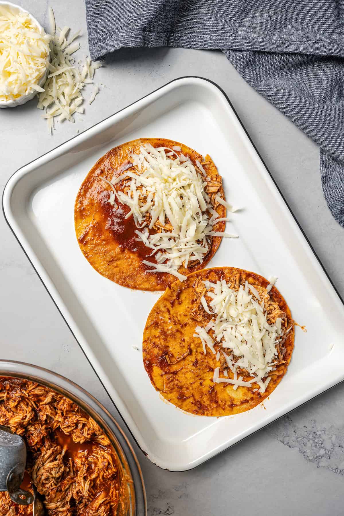 Two assembled chicken birria tacos topped with cheese on a baking tray.