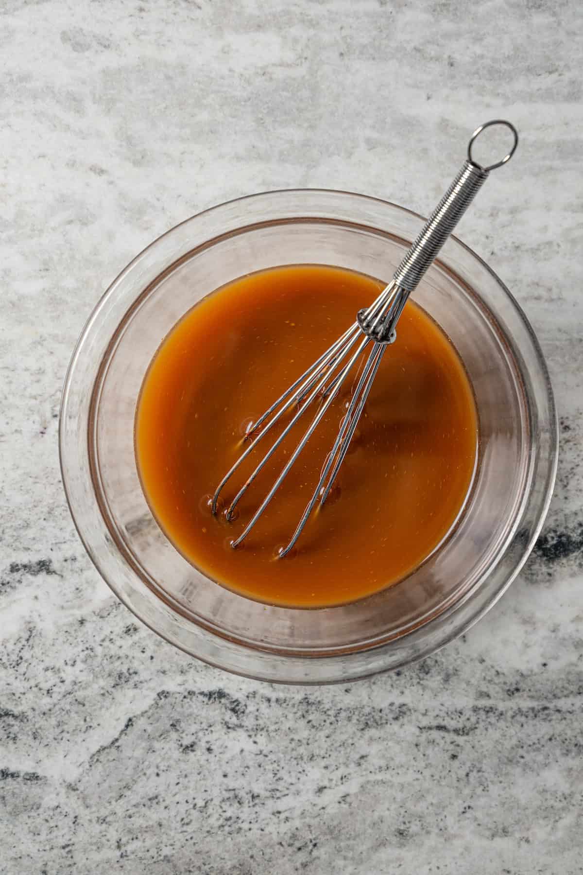 Empress chicken stir fry sauce in a glass bowl with a whisk.