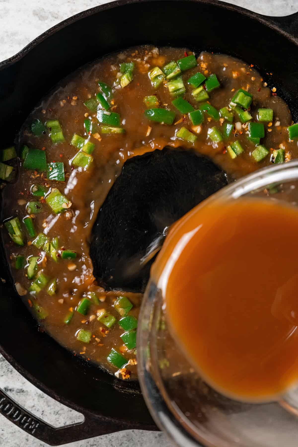 Stir fry sauce being poured over the sautéed onions, jalapeño, and garlic in a skillet.