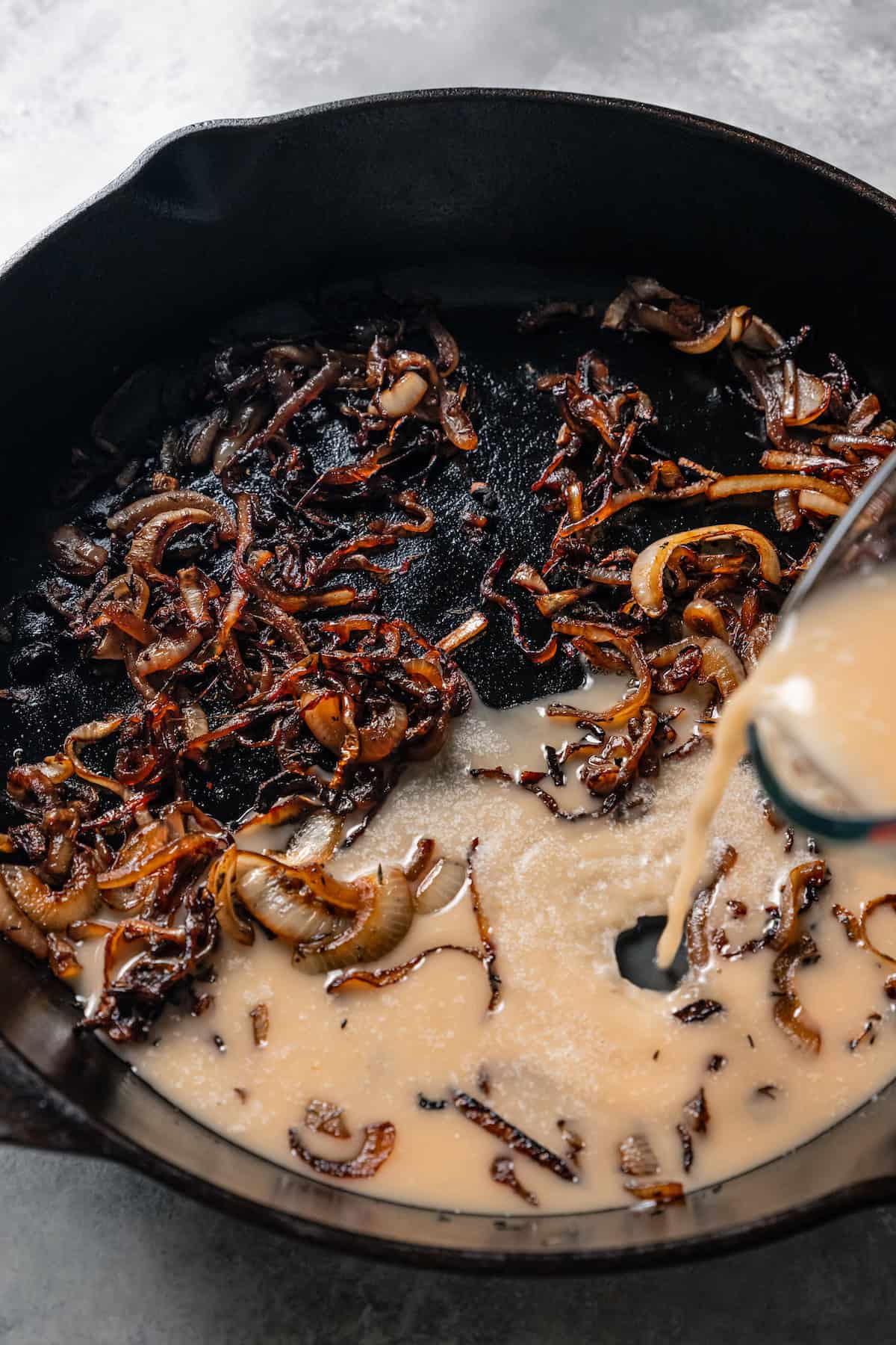 A slurry of cornstarch and beef broth being poured into a skillet of French onion soup.