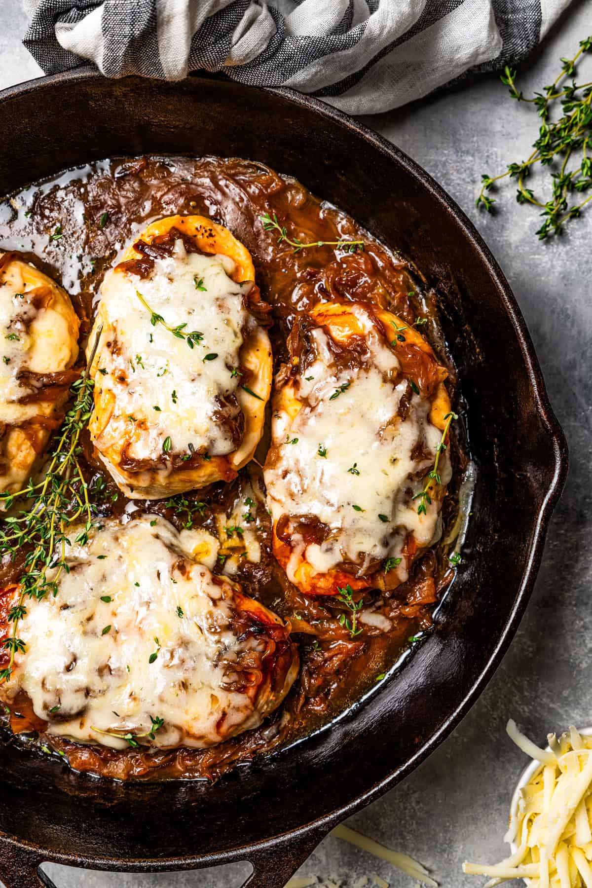 A skillet with four chicken breasts topped with caramelized onions and melted cheese.