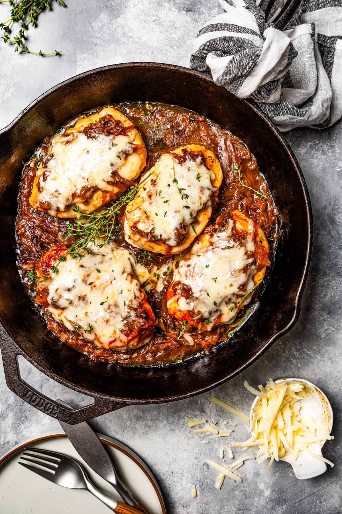 A skillet with French onion soup chicken topped with caramelized onions and melted cheese.