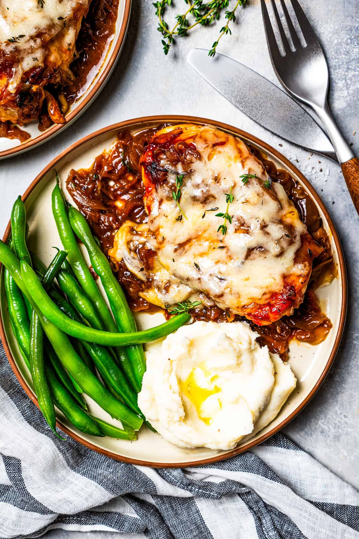 Overhead view of French onion chicken served on a plate with a side of green beans and mashed potatoes.