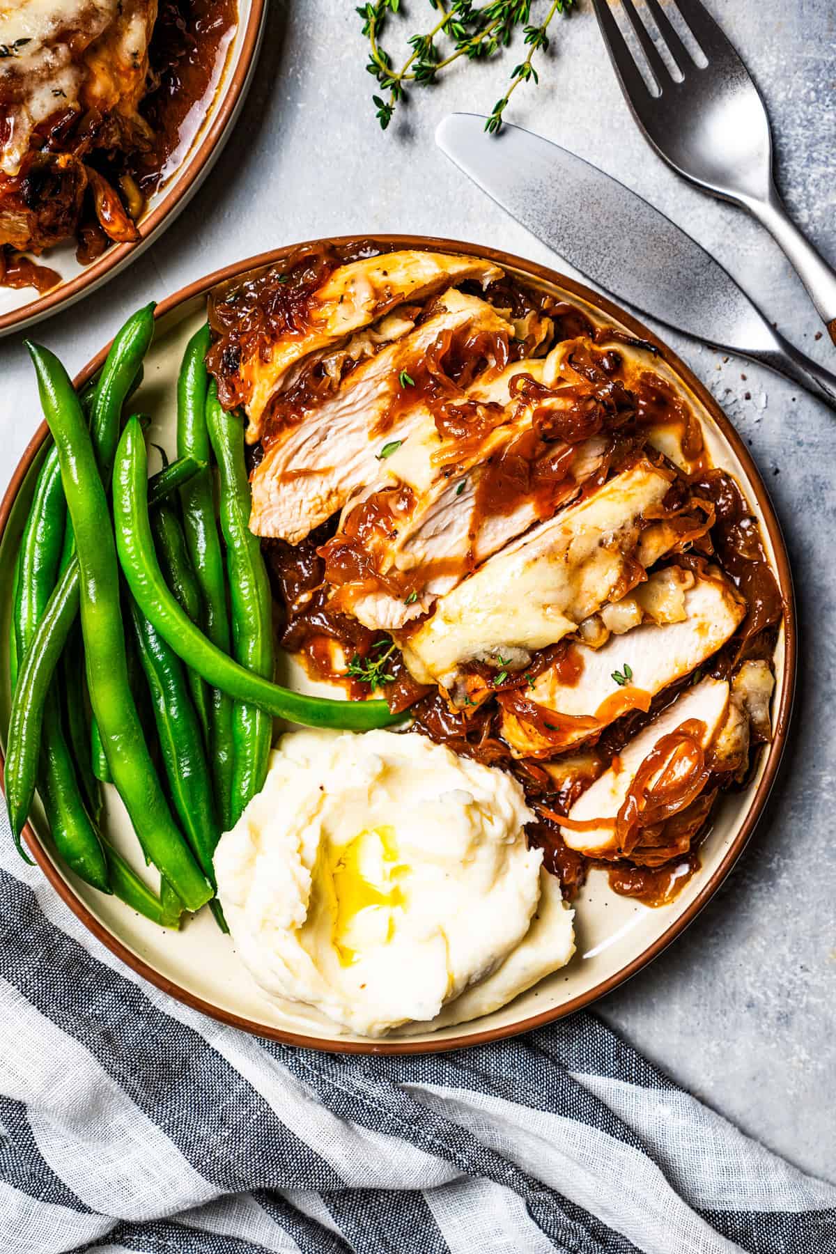 Overhead view of French onion soup chicken cut into slices on a plate with a side of green beans and mashed potatoes.