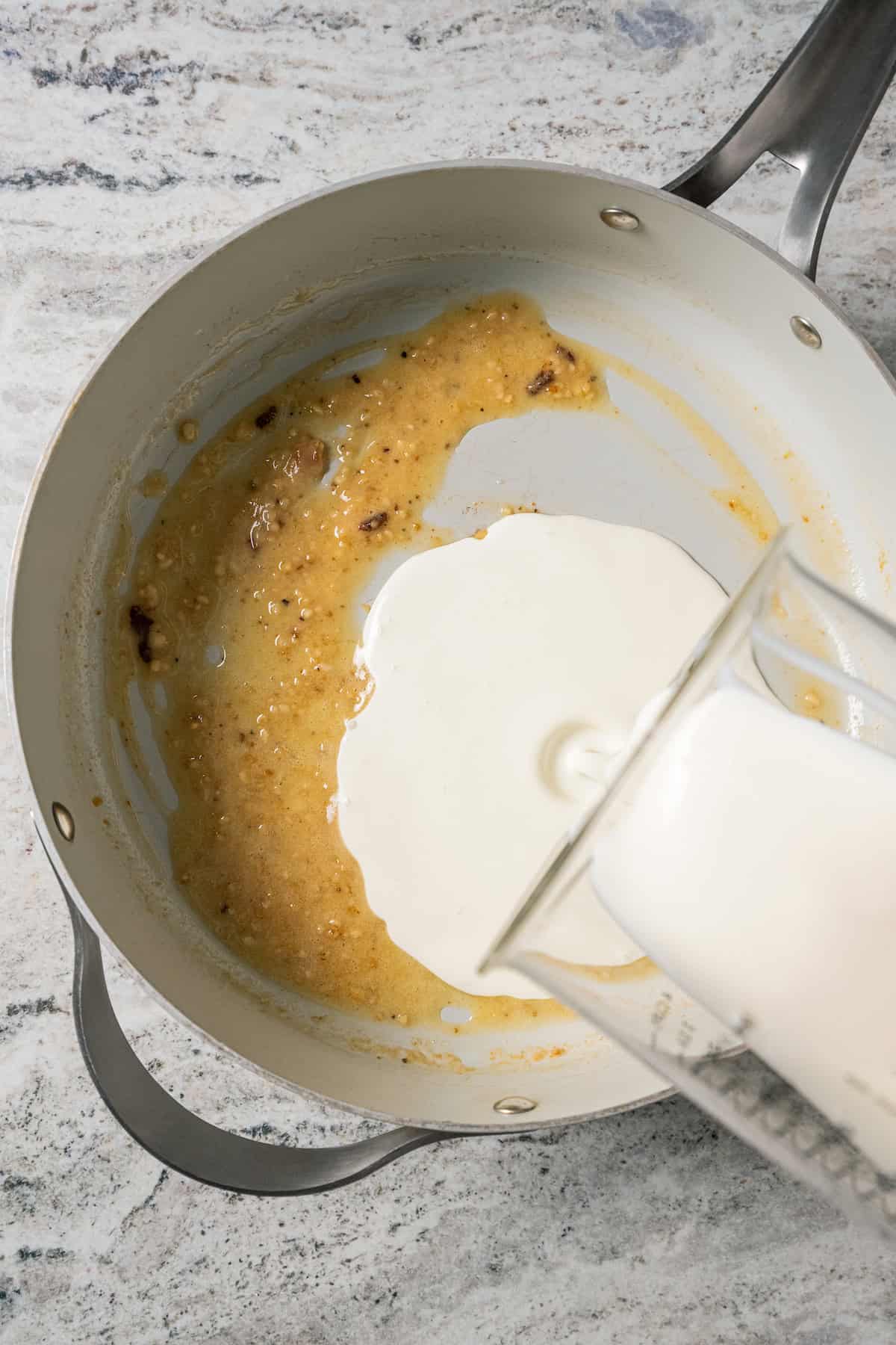 Heavy cream being poured over a roux of flour and butter in a skillet.