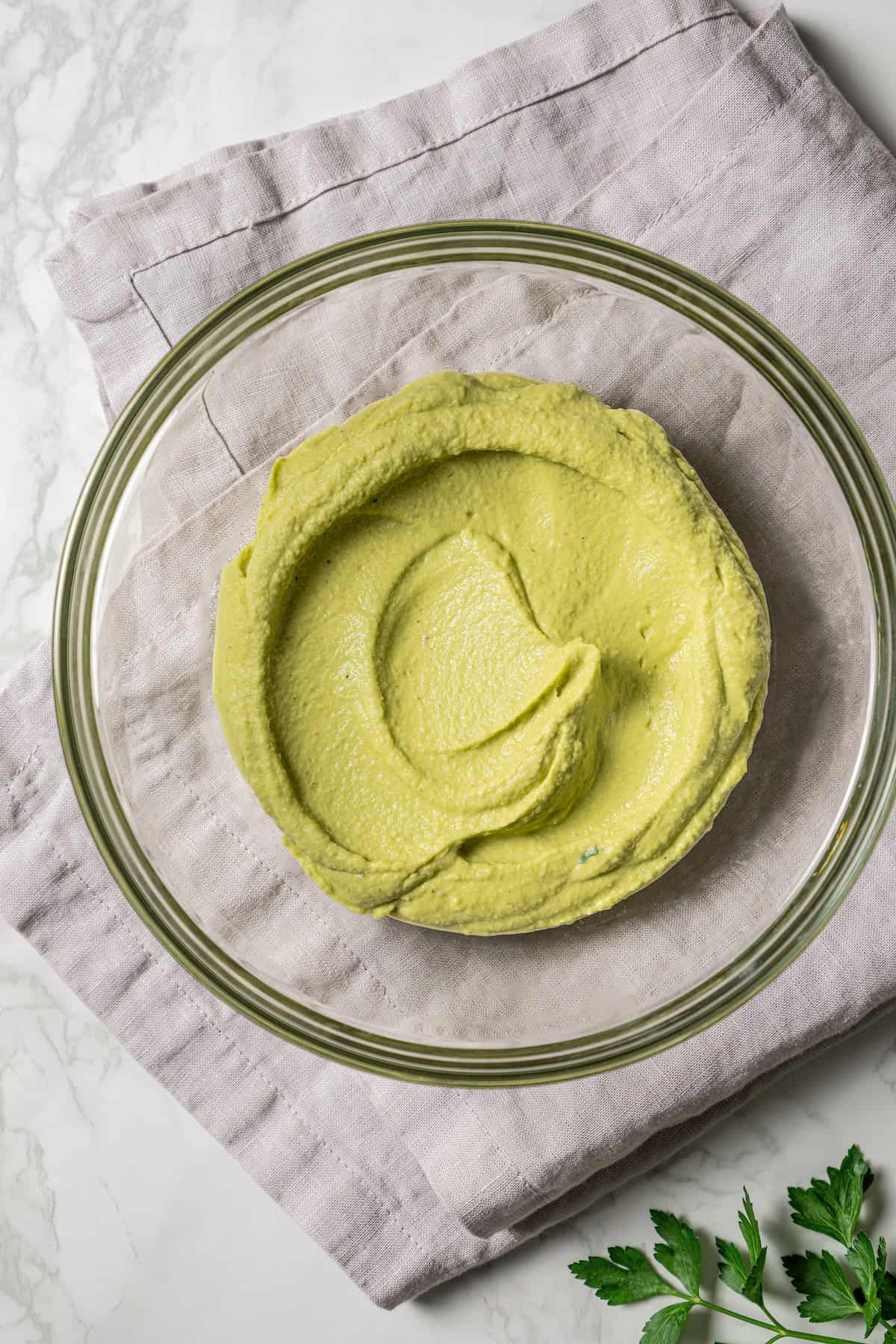 Creamy homemade hummus spread in the bottom of a glass bowl.