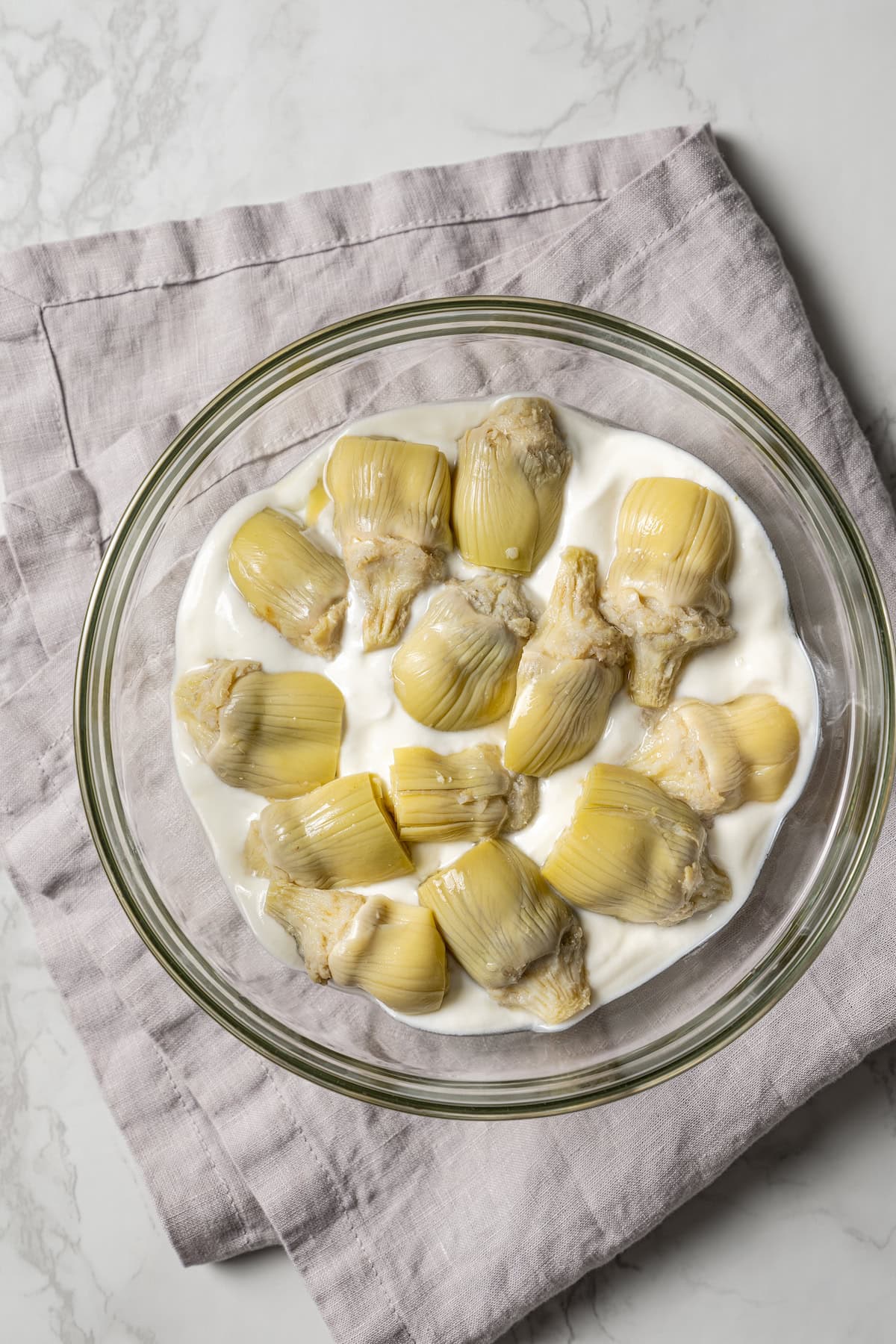 Artichoke hearts arranged over the hummus and yogurt layers in a glass bowl.