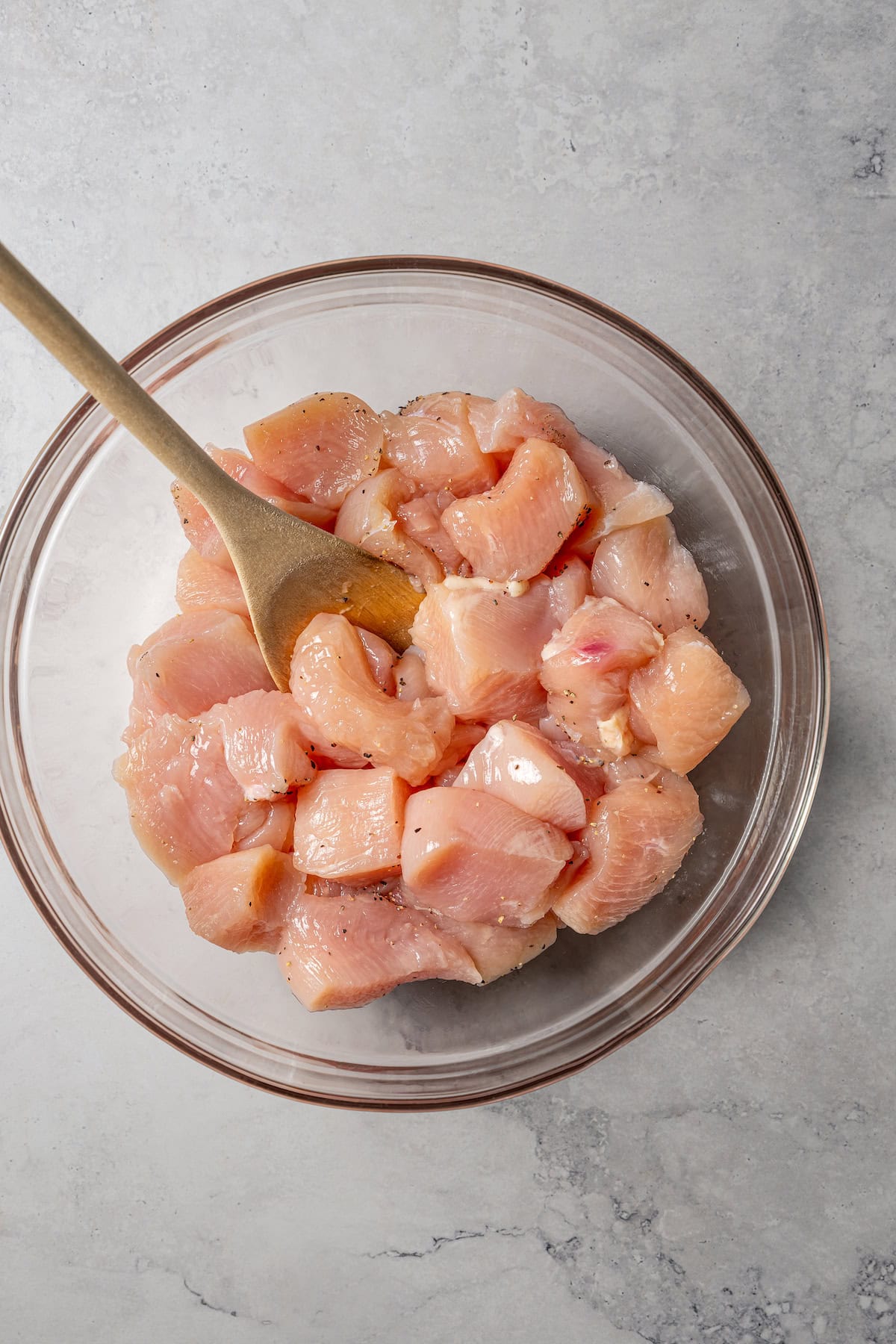 Seasoned cubed chicken in a glass bowl with a wooden spoon.