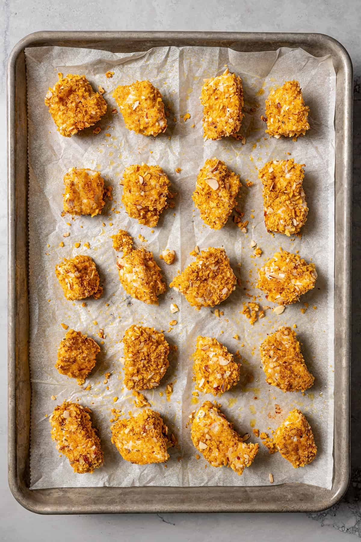 Baked pecan crusted chicken pieces on a parchment-lined baking sheet.