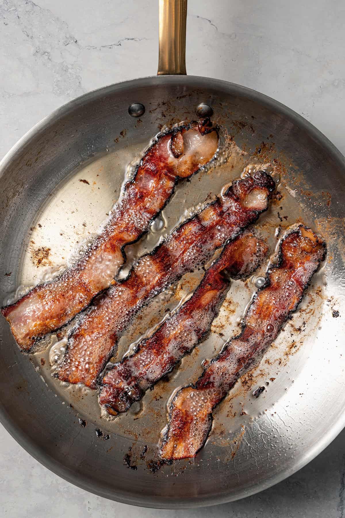 Cooked bacon sizzling in a metal skillet.