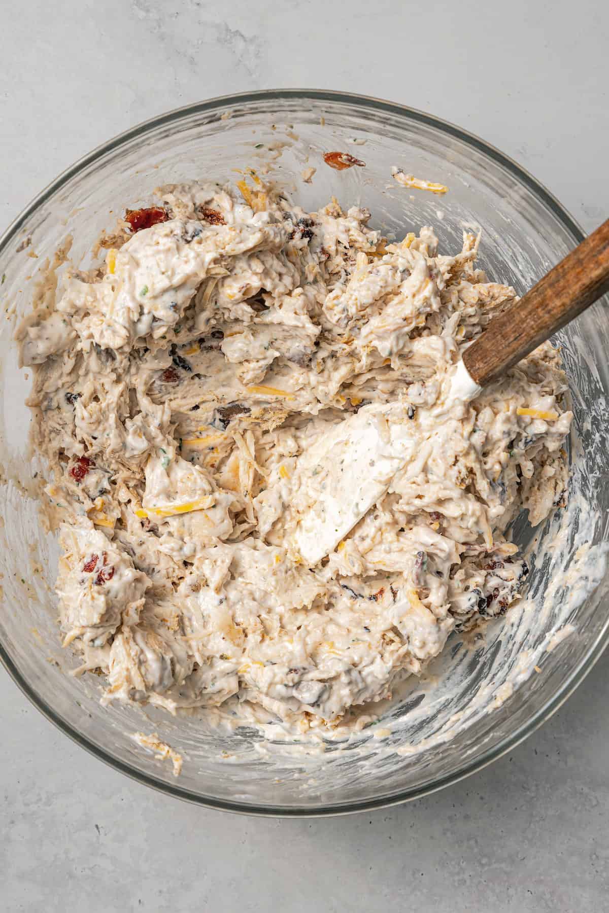 Chicken casserole filling in a glass bowl with a spatula.