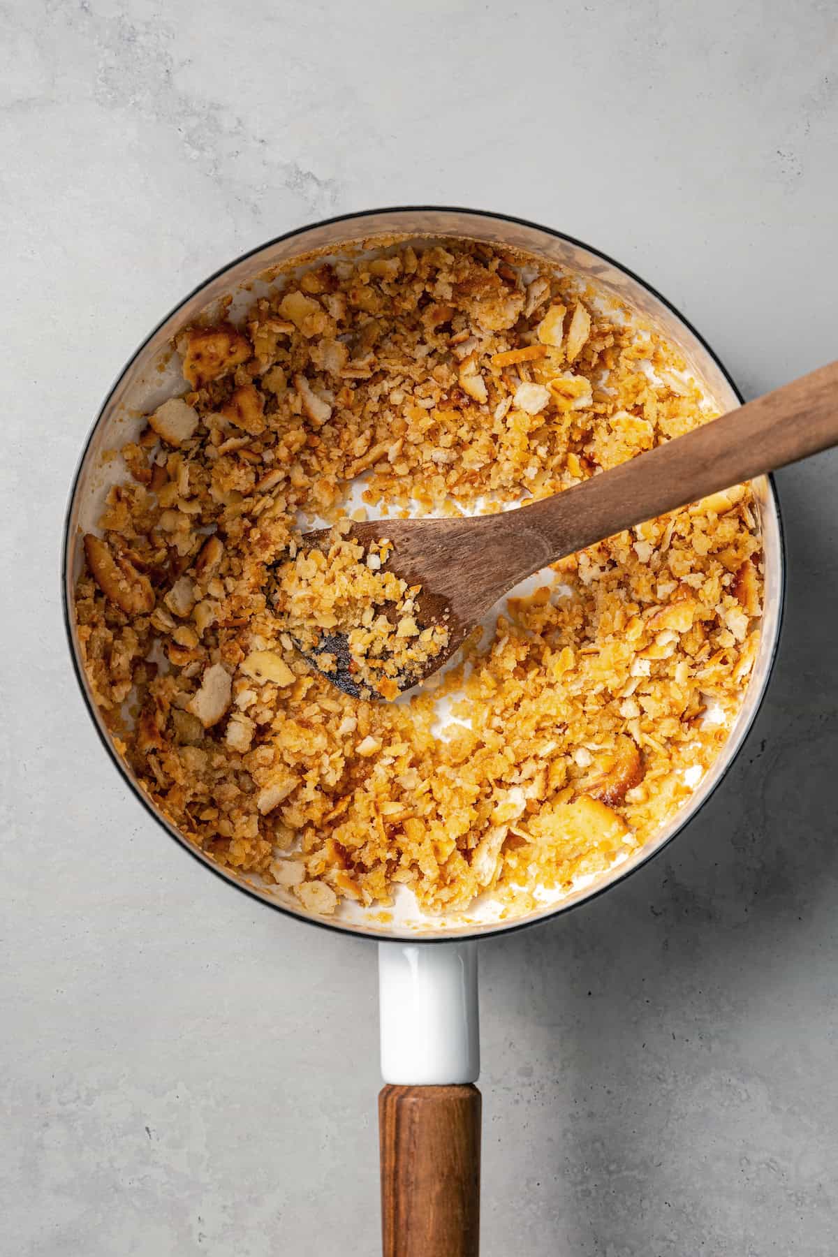 Ritz cracker crumb topping in a skillet with butter, being stirred by a wooden spoon.