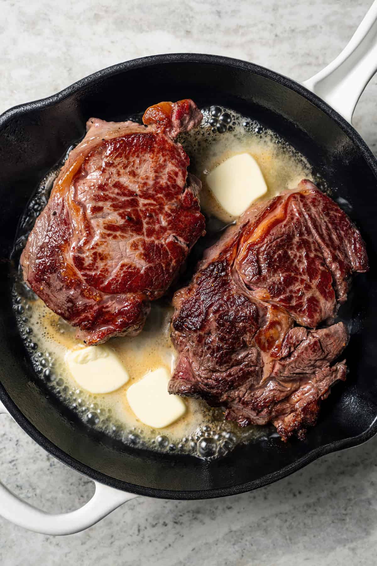 Two seared steaks with melting butter in a cast iron skillet.