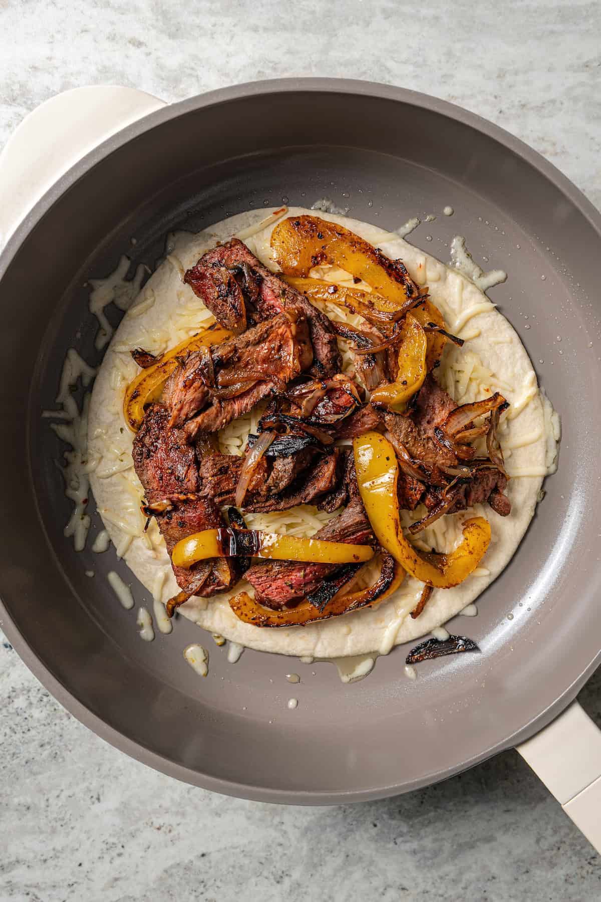 Steak filling layered over a flour tortilla in a skillet.