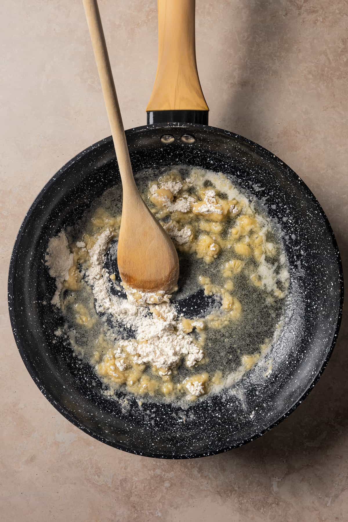 Flour cooking with butter in a skillet with a wooden spoon, to make a roux.