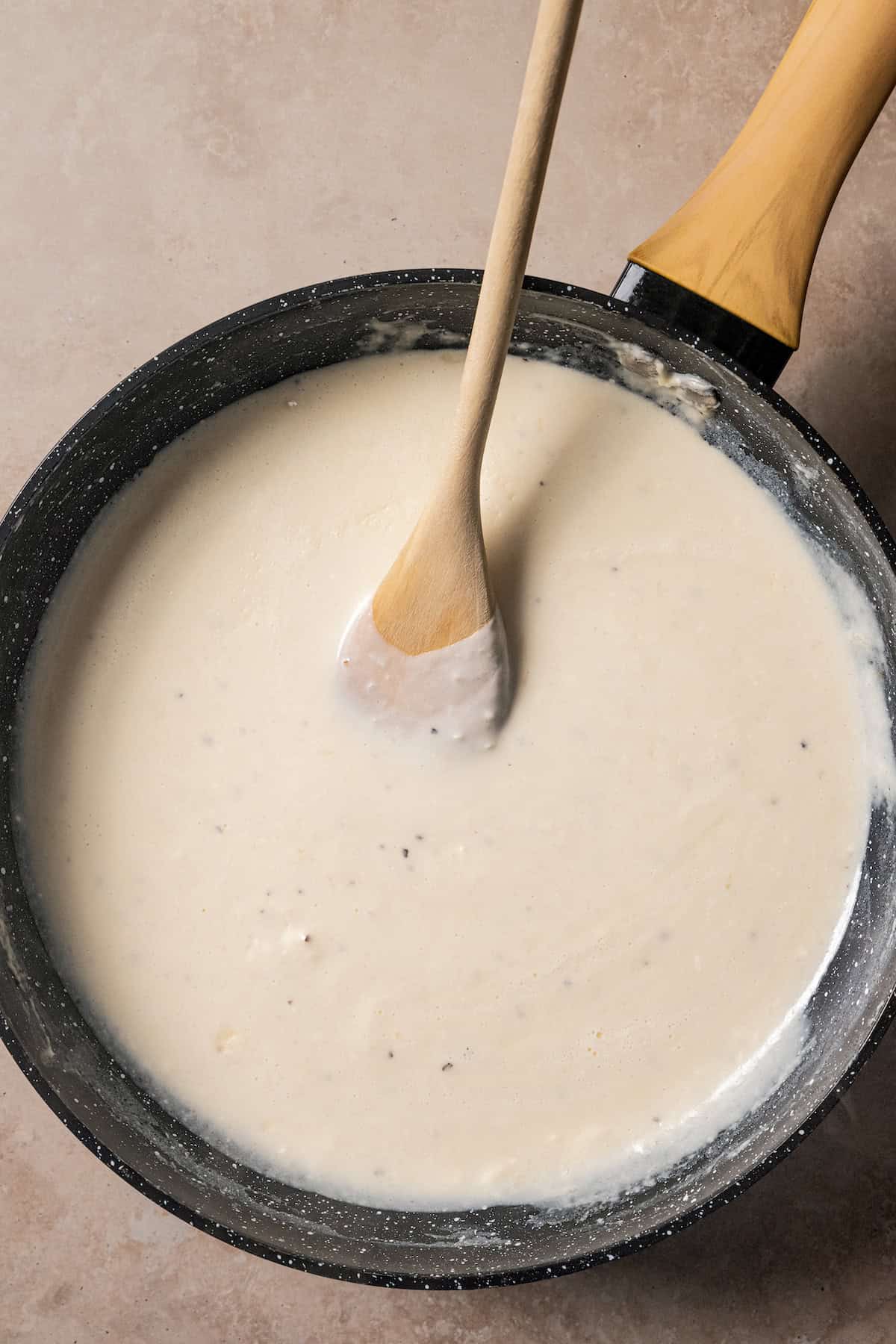 Béchamel sauce in a skillet with a wooden spoon.