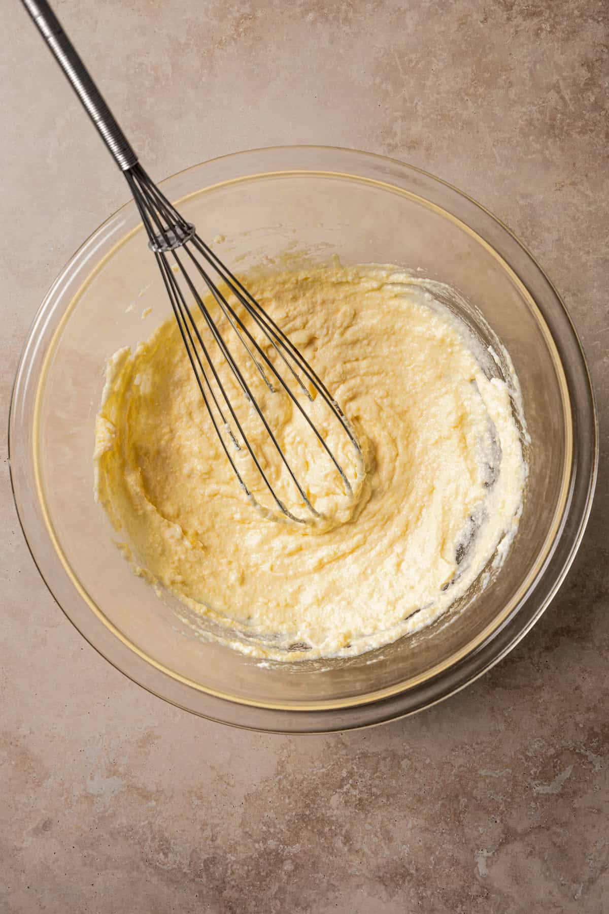 Cheese mixture in a glass bowl with a whisk.