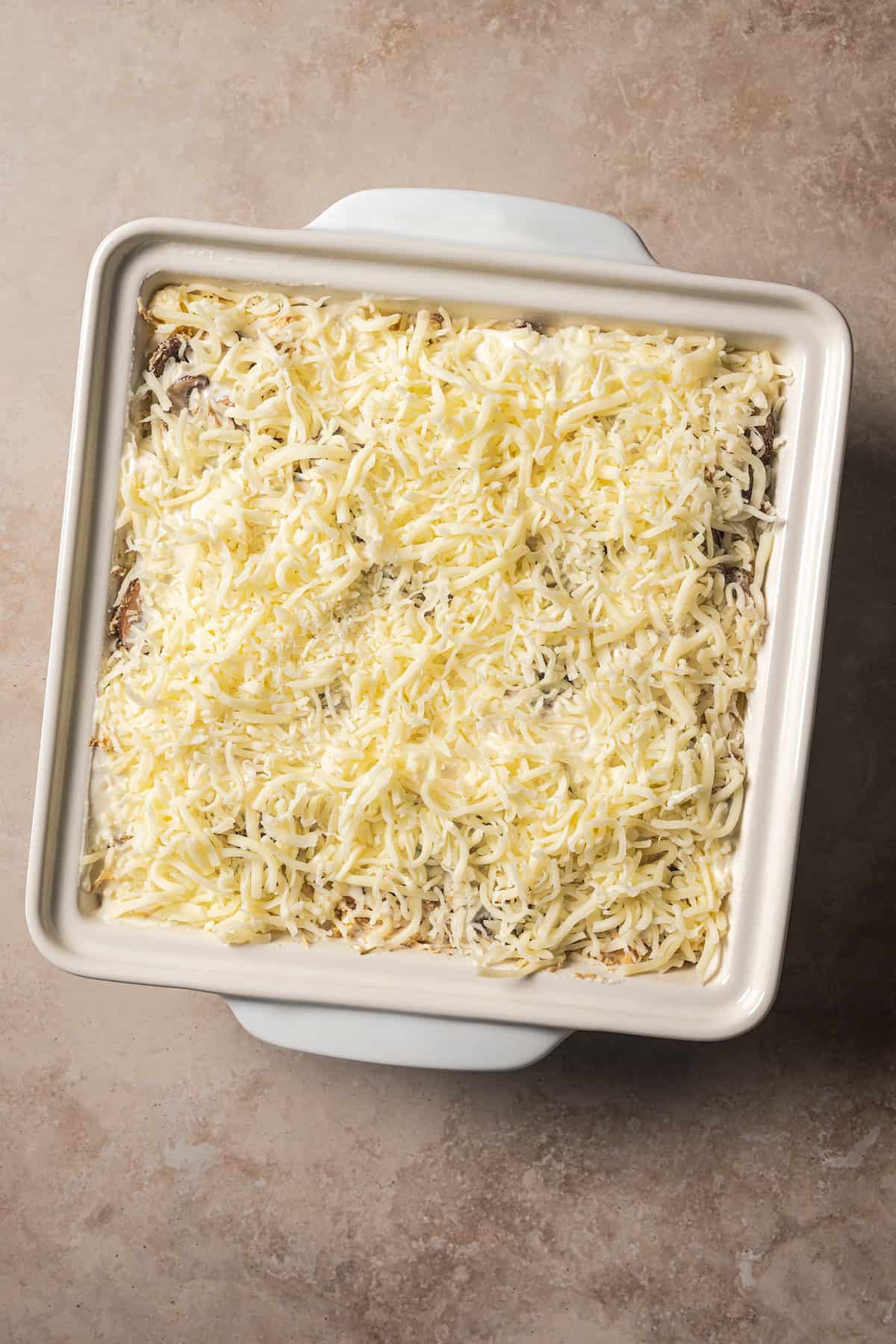 Assembled white chicken lasagna topped with shredded cheese in a baking dish.