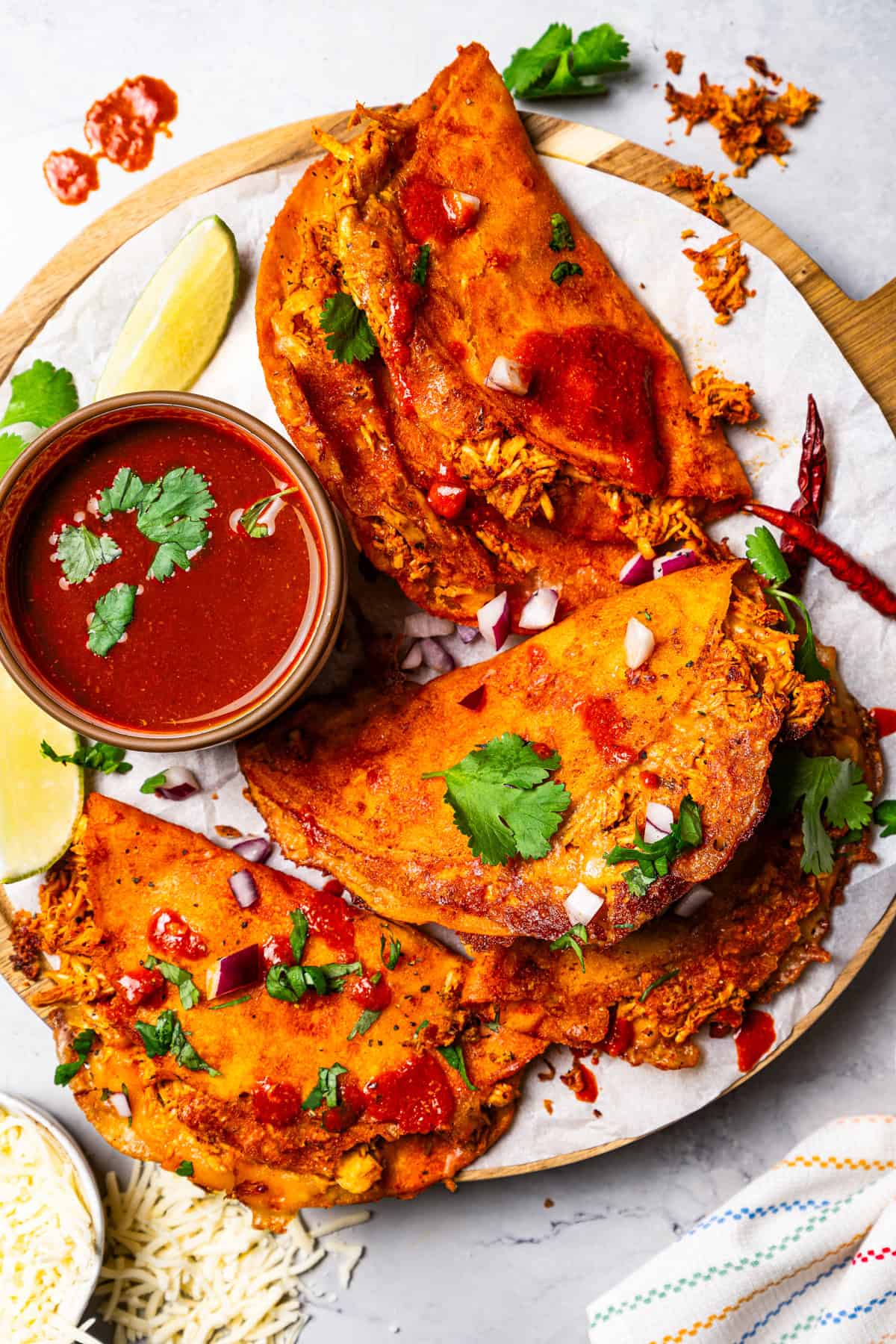 Overhead view of chicken birria tacos arranged around a small bowl of consomme on a round wooden platter.