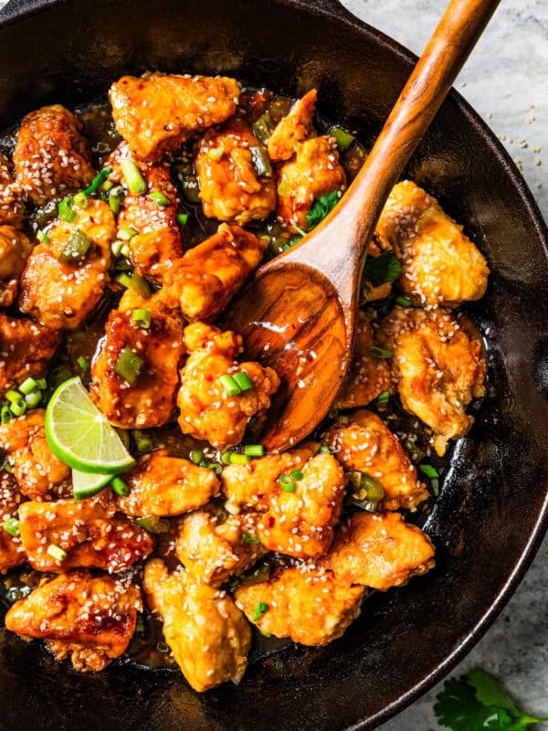 Wooden spoon stirring through diced cooked chicken in a skillet, garnished with fresh herbs and a lime wedge.