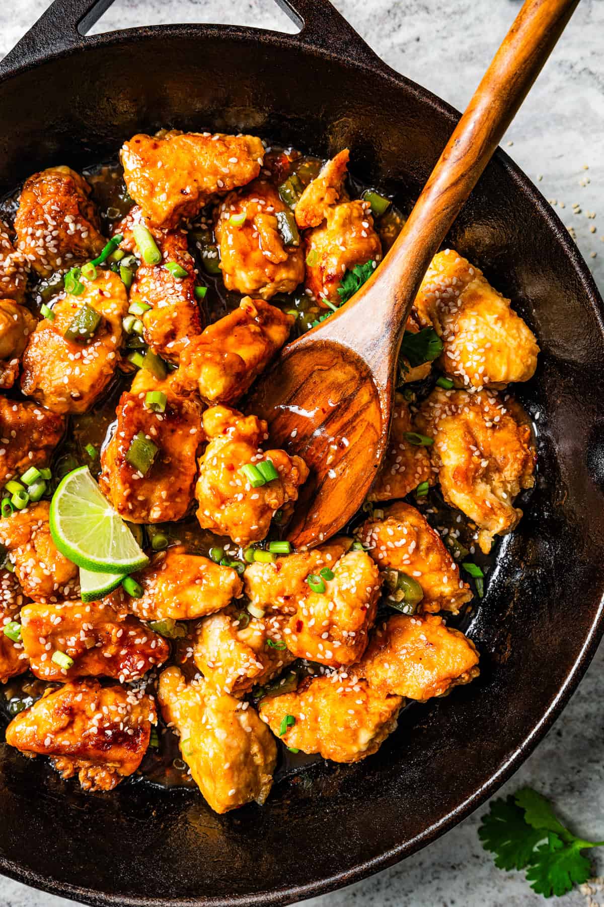 Wooden spoon stirring through diced cooked chicken in a skillet, garnished with fresh herbs and a lime wedge.