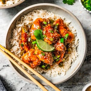 Empress chicken served over a bowl of white rice with a pair of chopsticks resting on the edge of the bowl.