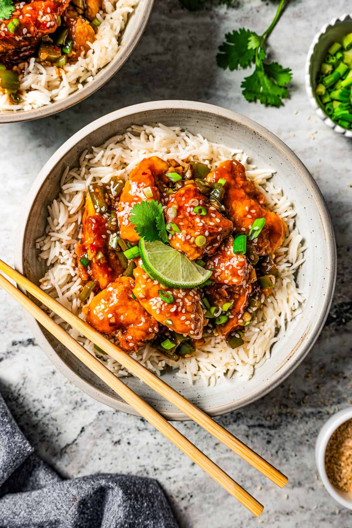 Empress chicken served over a bowl of white rice with a pair of chopsticks resting on the edge of the bowl.