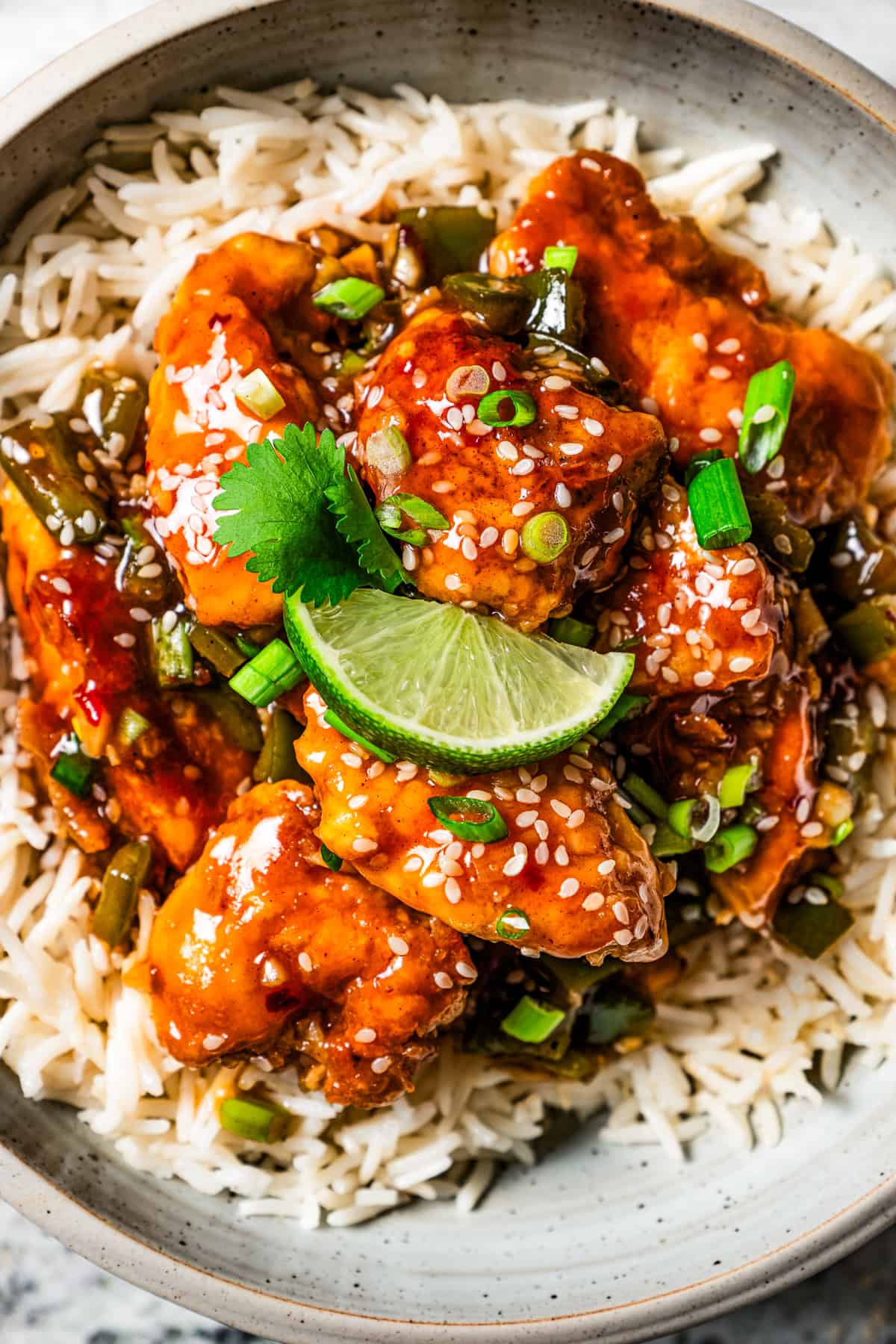 Close up overhead view of empress chicken served over rice, garnished with a lime wedge, sesame seeds, and green onions.